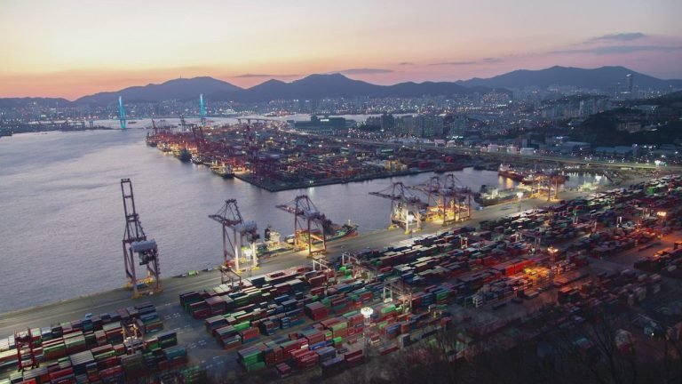Aerial view of a container port at dusk, cranes lined along the quay