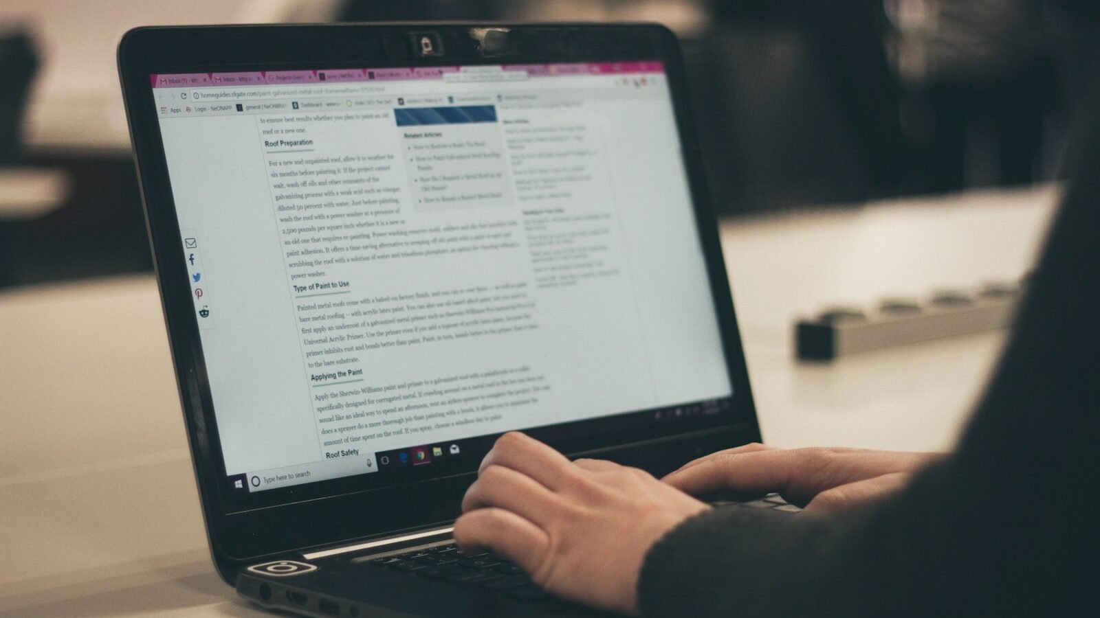 A person typing on a laptop that shows a long web article.